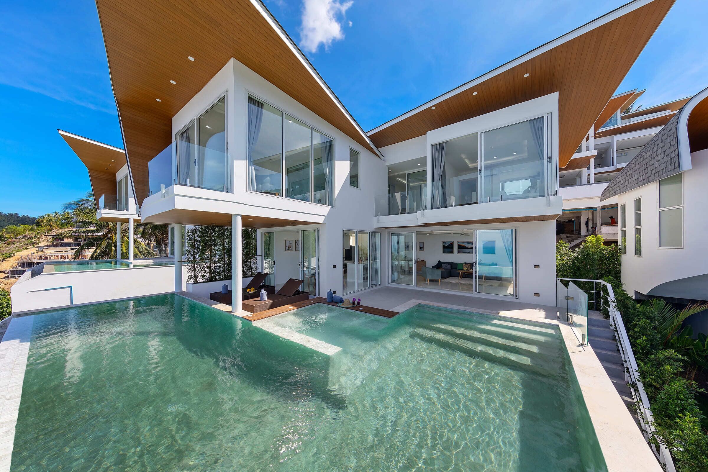Una casa moderna con una piscina grande, varios balcones y amplias ventanas.