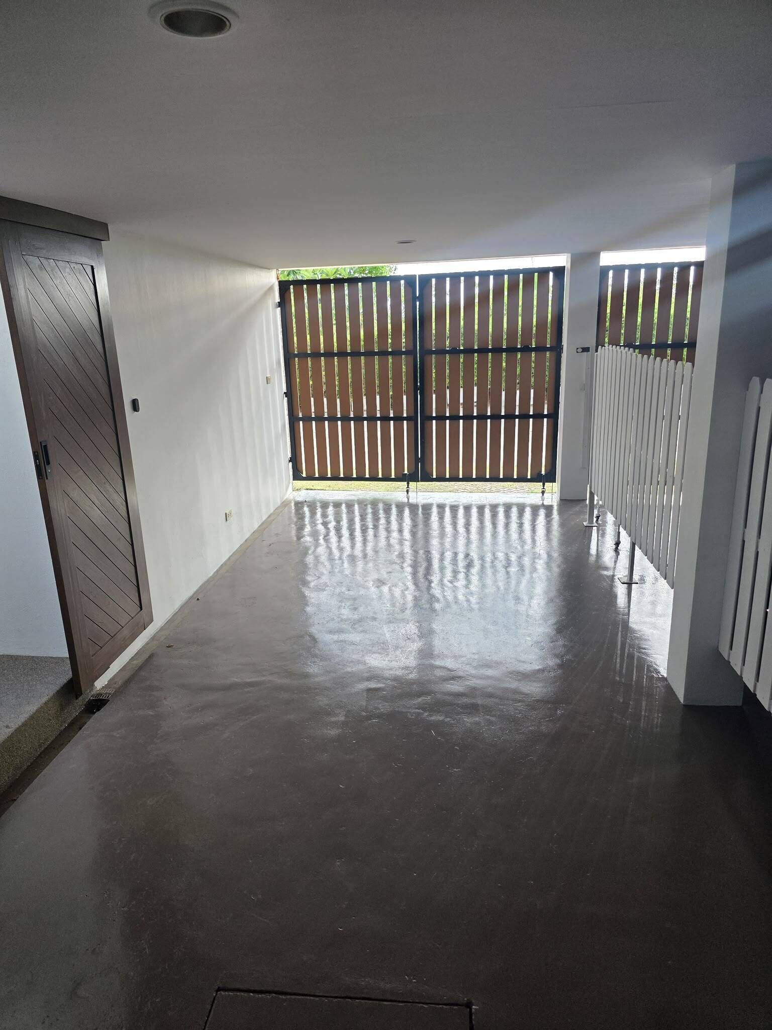 A spacious indoor area with a concrete floor, a sliding door, and a metal gate leading outside.