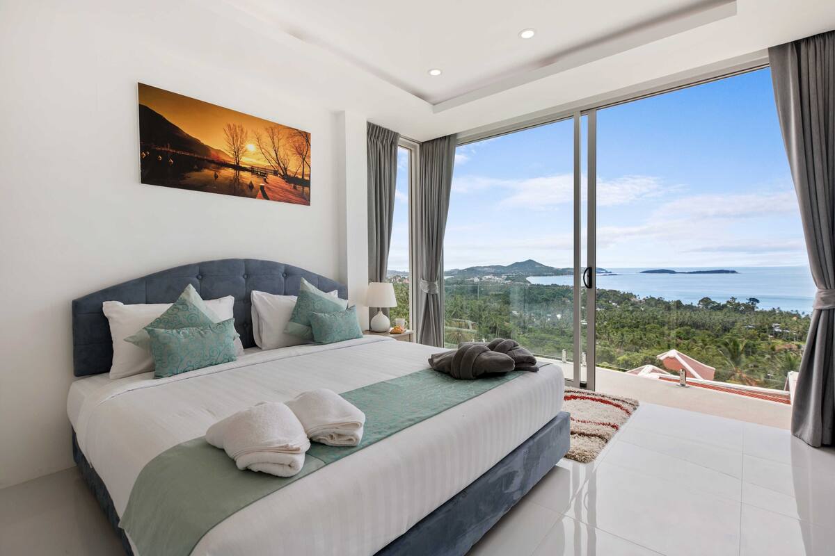 A bedroom with a large bed, a view of the sea, and a painting on the wall.