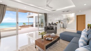 A modern living room with a large sofa, a coffee table, and a view of the ocean through floor-to-ceiling glass doors. - Villa the wave (Koh Samui)