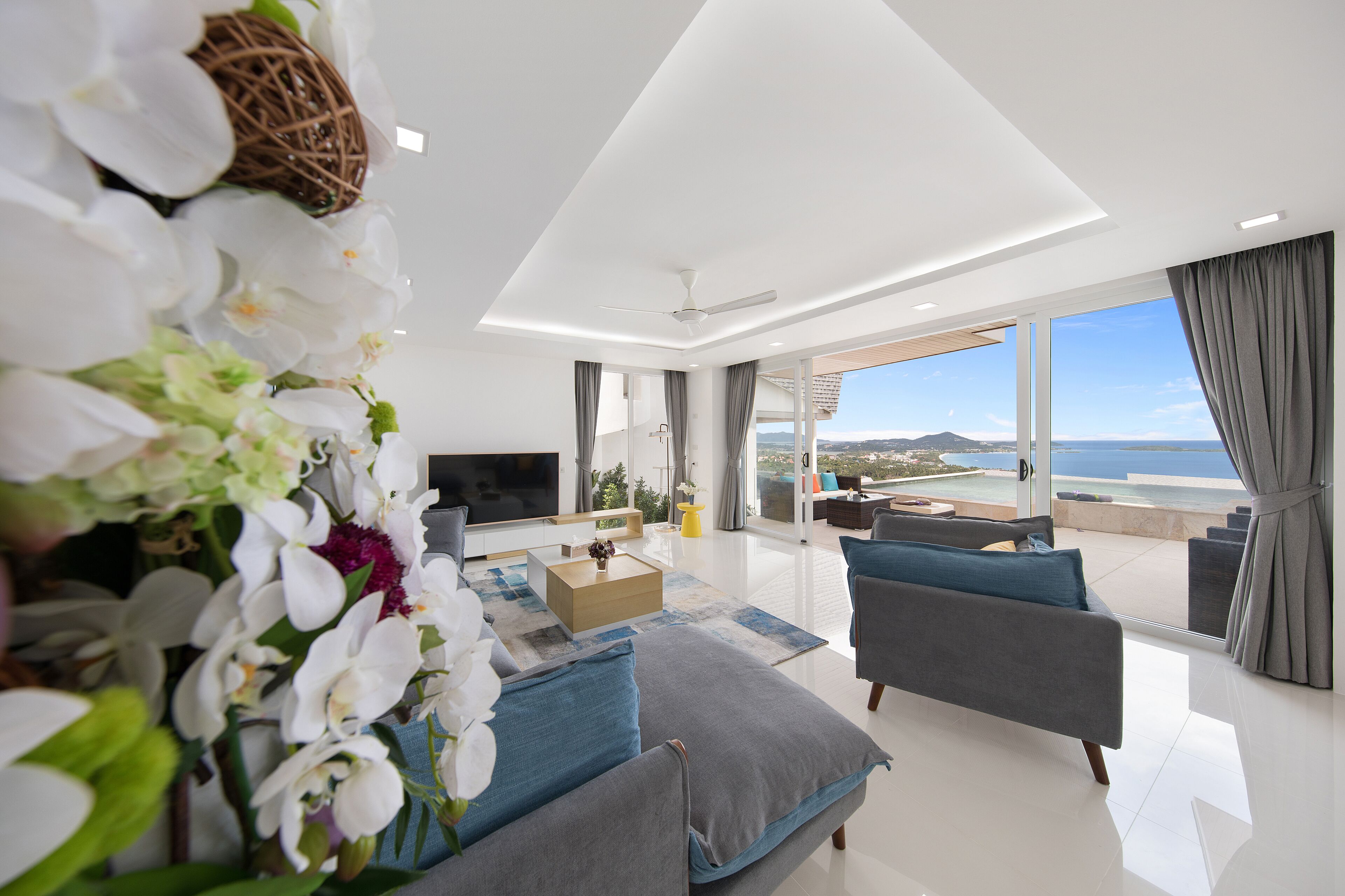 Un salon moderne avec un téléviseur à écran plat, une table basse et un canapé. Une grande fenêtre offre une vue sur la mer.