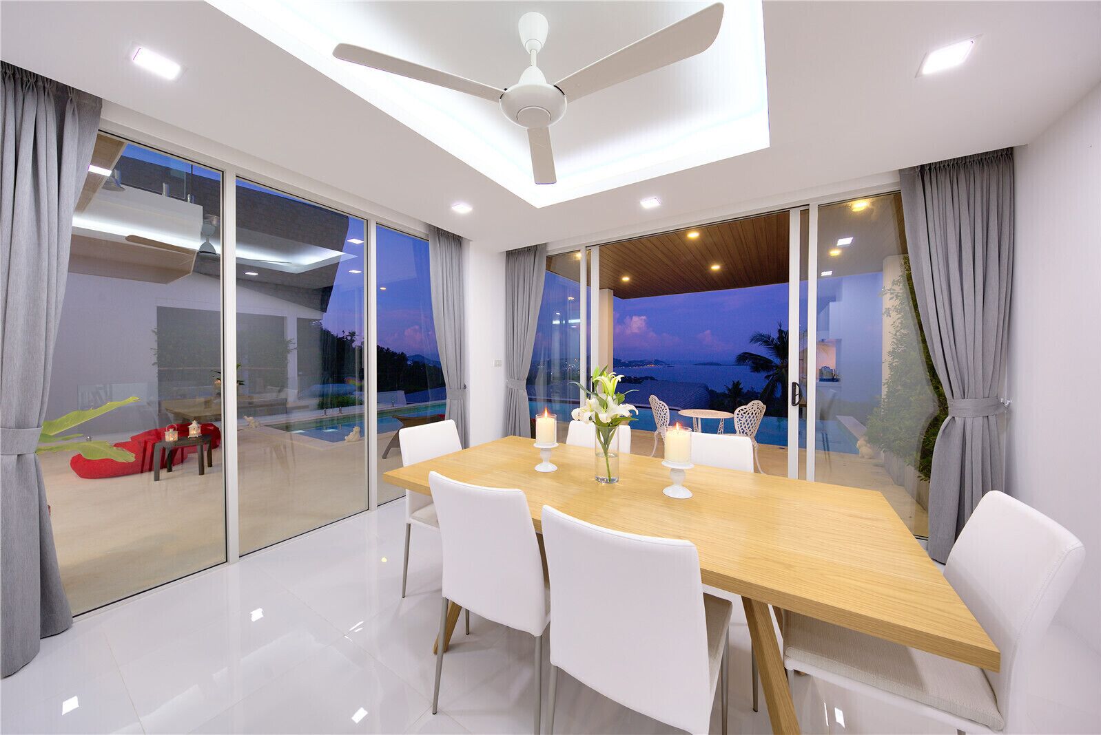 A modern dining area with a large table, white chairs, and a view of the ocean.