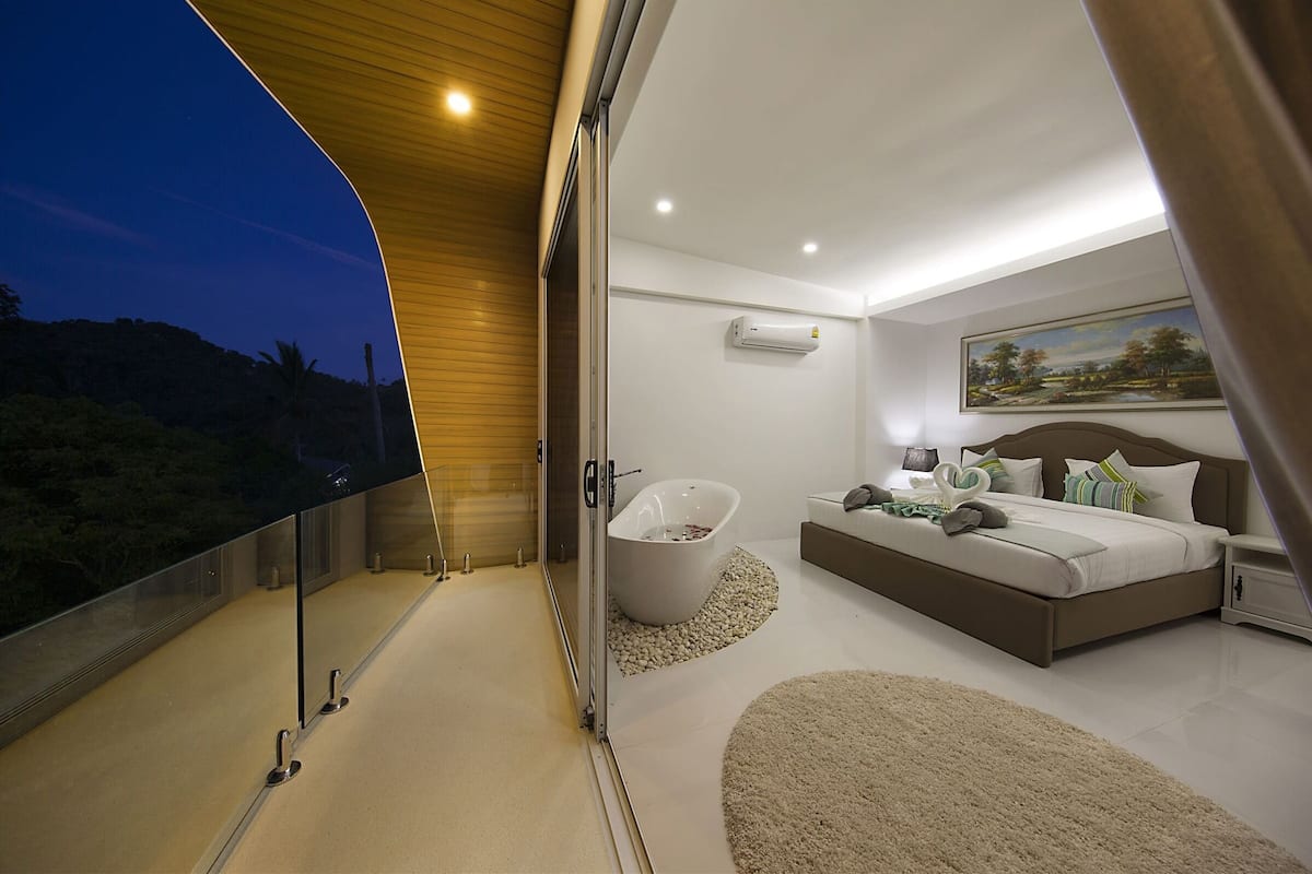 A modern bedroom with a large bed, a bathtub, and a balcony with a view of the landscape.