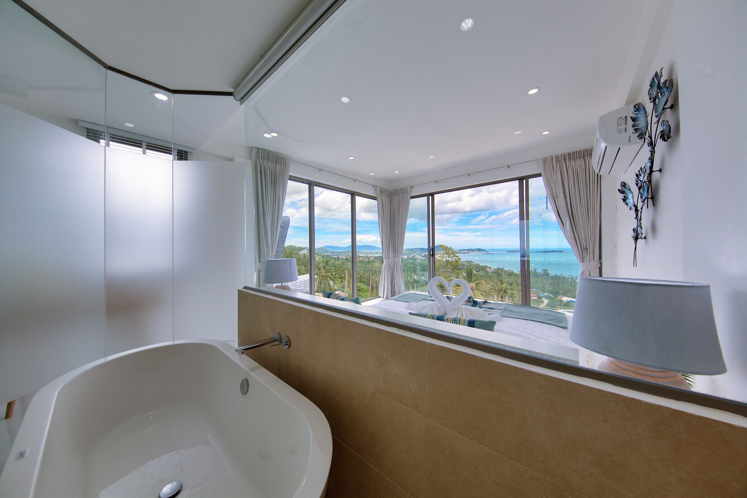A modern bathroom with a large bathtub, a view of the ocean, and a window with curtains.