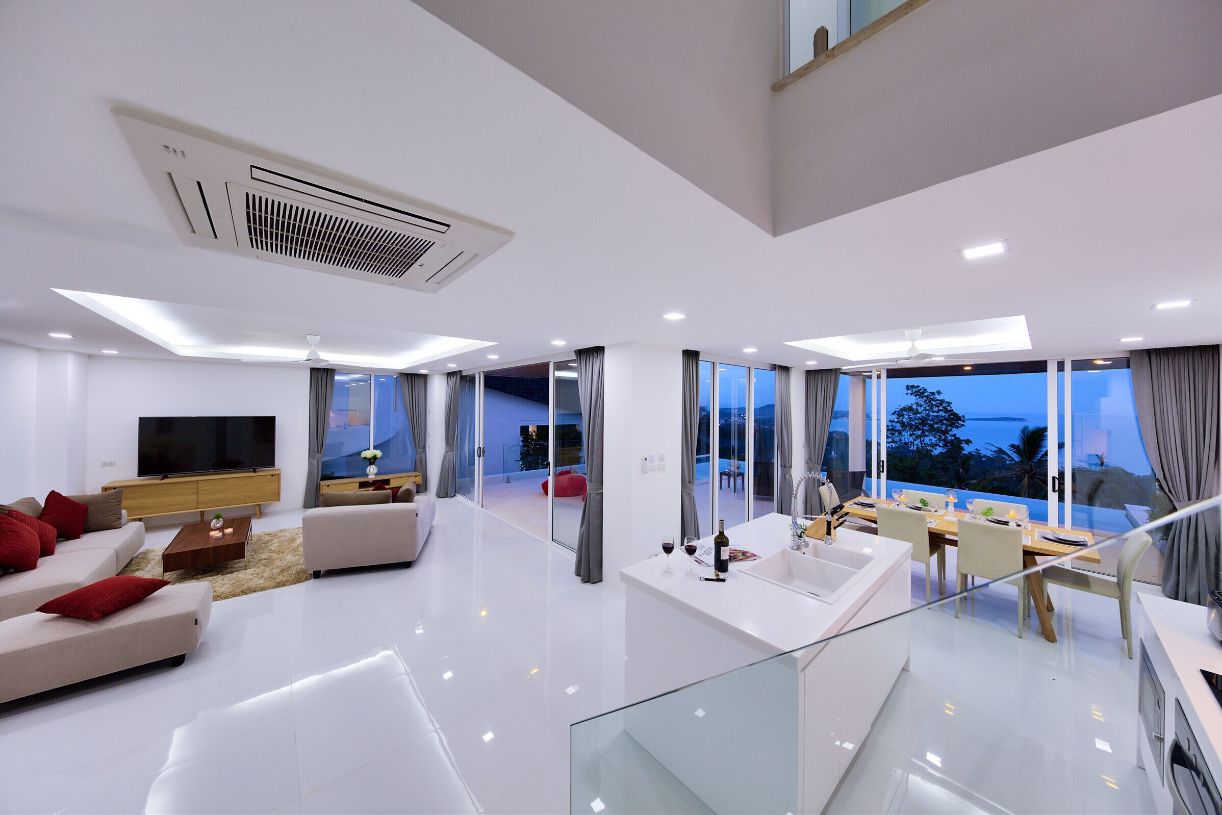 Una sala de estar moderna con televisor de pantalla plana, sofá y comedor con barandilla de vidrio.