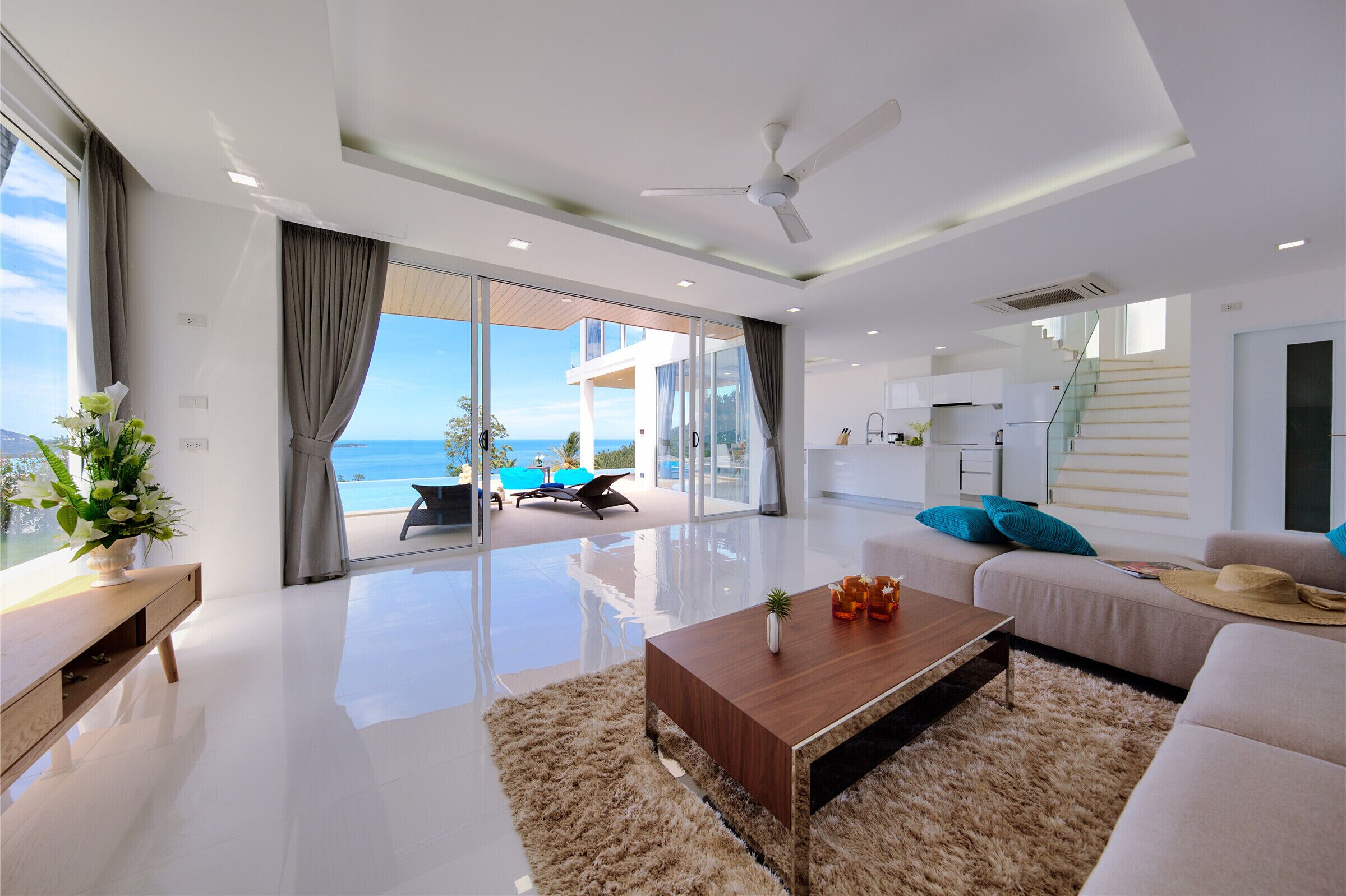 A modern living room with a large glass door leading to a balcony with a view of the sea.