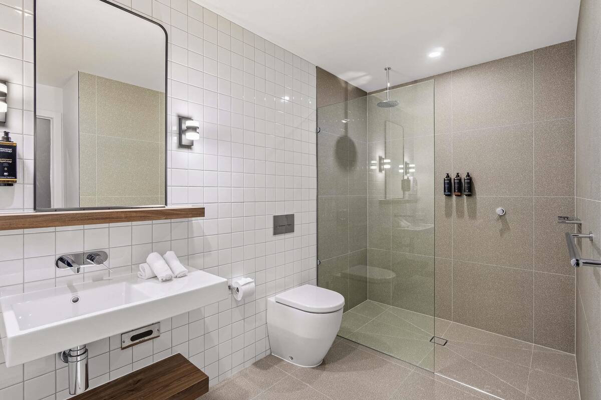 Une salle de bain moderne avec un lavabo blanc, un miroir, des toilettes et une douche à parois de verre.