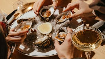 Un groupe de personnes est réuni autour d’une table, dégustant des huîtres présentées dans une assiette, accompagnées d’un verre de vin blanc.