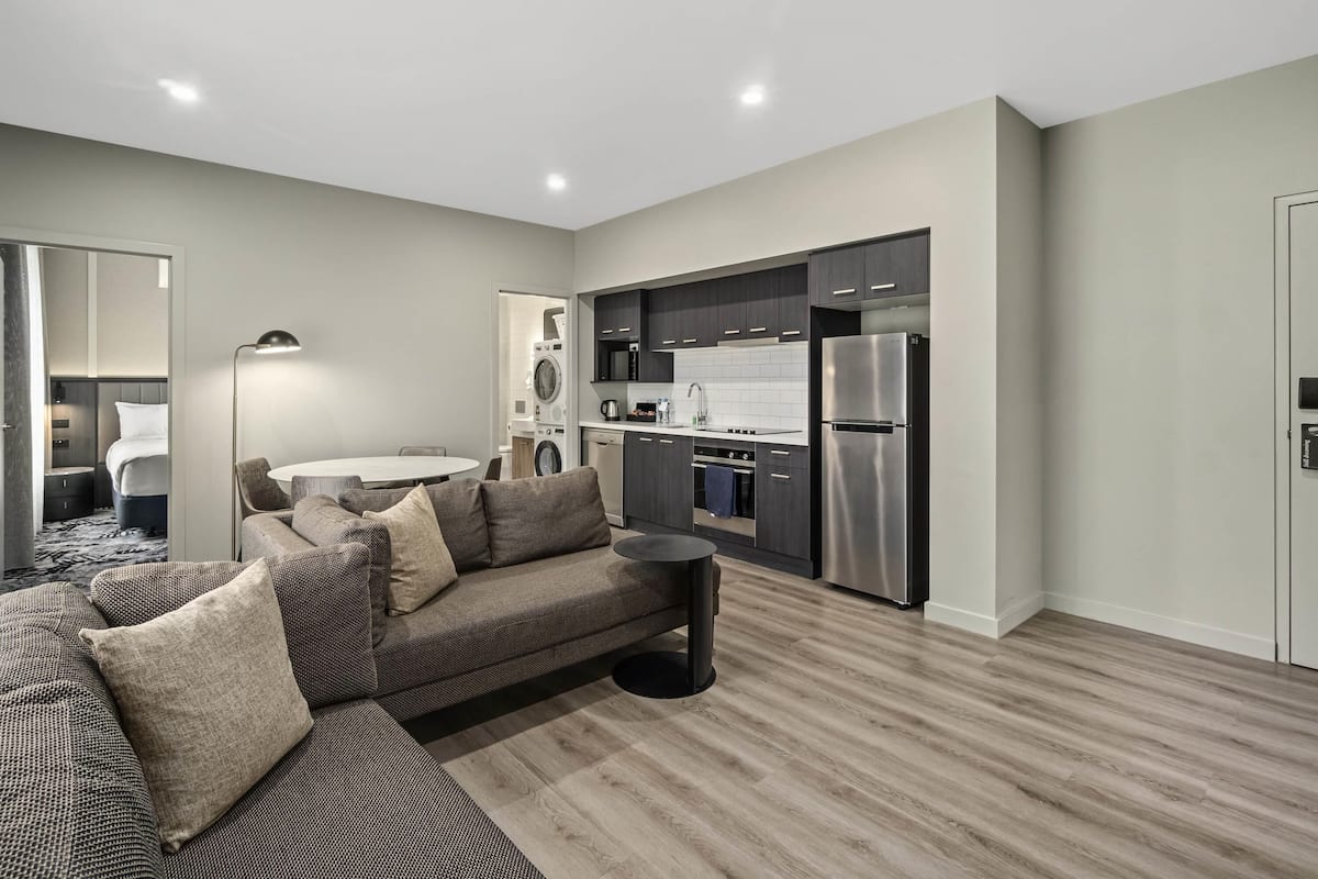 A modern living room with a sofa, a dining table, and a kitchen area with appliances.