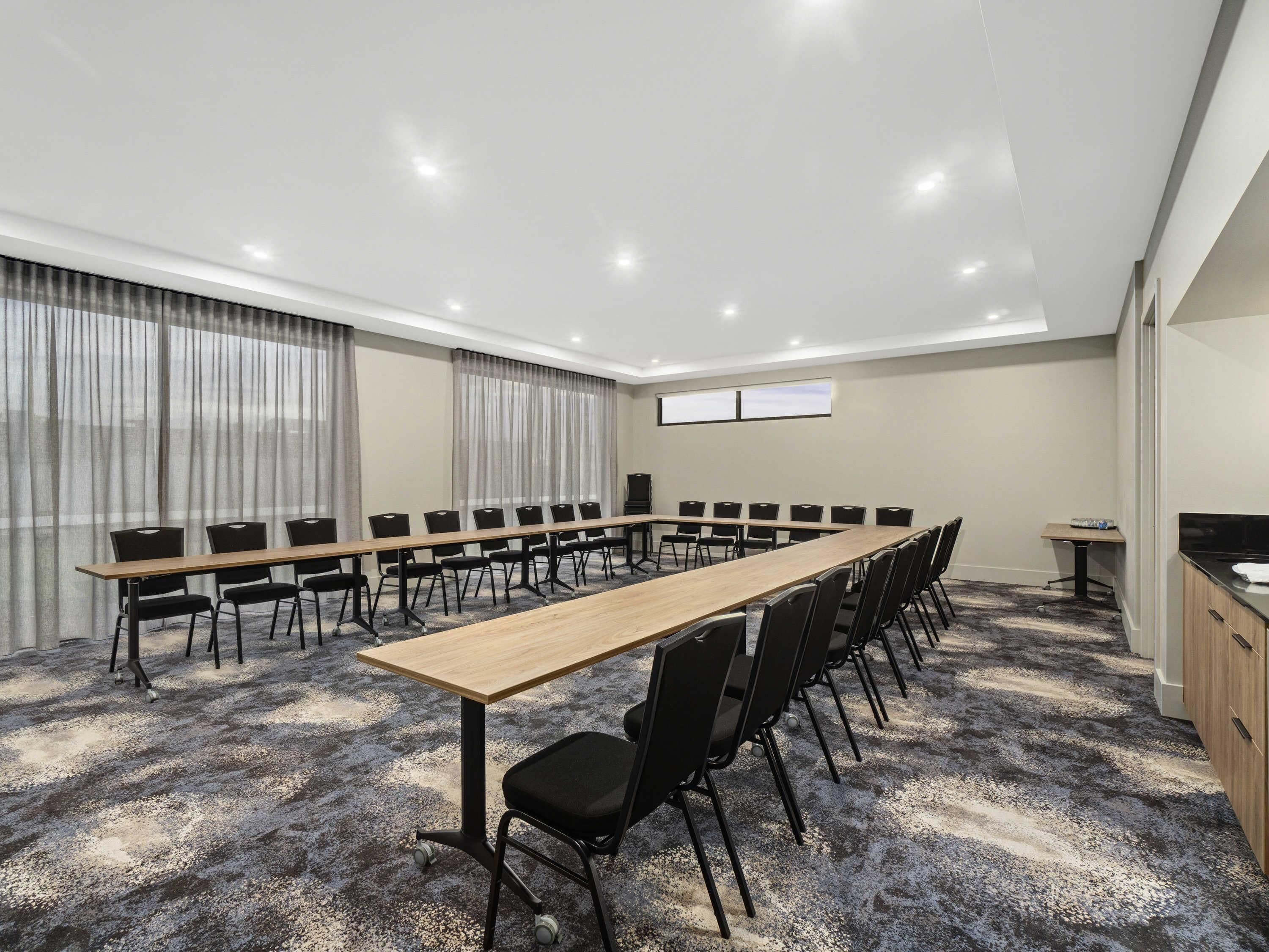 A conference room with a long table, black chairs, a TV screen, and a carpeted floor.