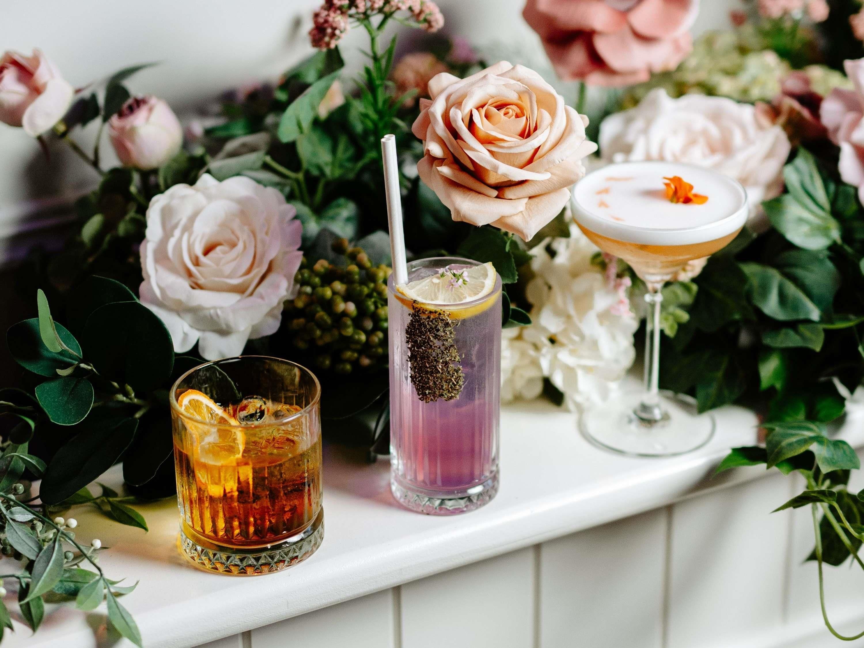 Tre glas med drikkevarer på en hylde med blomster baggrund.