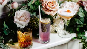 Tre glas med drikkevarer på en hylde med blomster baggrund.
