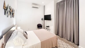 A modern hotel room with a bed, a flat-screen TV, an air conditioning unit, and a large window with curtains.