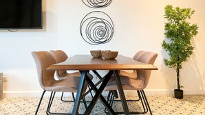 A dining area with a wooden table, cushioned chairs, a woven basket, and a potted plant.