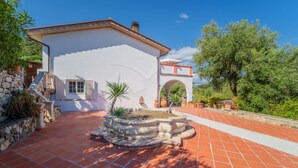 A white building with a tiled patio, stone walls, and a fountain. - LA PALAZZINA NEL VERDE - PALAZZINA NEL VERDE N° 2 (Campo nell'Elba)