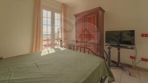 A bedroom with a bed, a television on a stand, a wardrobe, and a window with curtains.