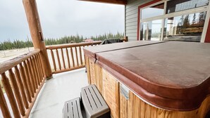 A wooden deck with a hot tub, a wooden railing, and a view of the beach and trees. - Luxurious TRUE ski in/out chalet in Happy Valley with gorgeous views! (Beaverdell)