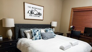 A neatly made bed with a white comforter and blue patterned pillows, a framed motivational quote on the wall, and a wooden desk with a laptop and a vase of flowers. - Luxurious TRUE ski in/out chalet in Happy Valley with gorgeous views! (Beaverdell)