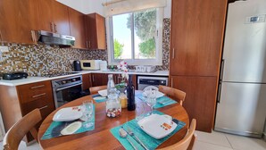Une cuisine moderne avec des meubles en bois, un réfrigérateur en acier inoxydable et une table à manger pour quatre personnes, agrémentée de sets de table et de couverts.
