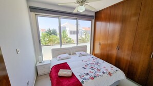 Une chambre à coucher avec un lit, un ventilateur de plafond, une fenêtre et une armoire.