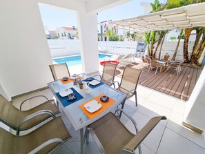 Dine al fresco under a shaded pergola with a clear view of the pool and lush garden.