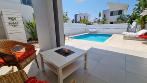 Un espace extérieur moderne doté d’une piscine, de chaises longues et d’une table blanche.