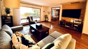 Amplia sala de estar con un televisor grande, asientos cómodos y un área de comedor visible a través de un arco.