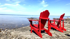 Dos sillas Adirondack rojas sobre una costa rocosa, con vista al agua y al cielo.