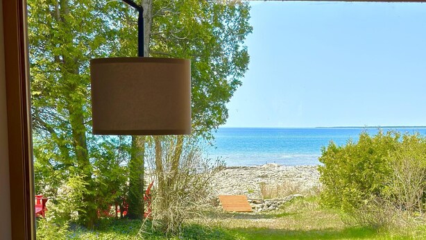 Una silla de mimbre con cojines color turquesa, una terraza de madera con sillas azules y vistas a la playa y al océano a través de amplias ventanas.