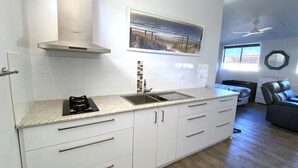 A modern kitchen with white cabinets, a stainless steel sink, and a gas stove. - Getaway Villas Unit 38-7 - comfort on a budget (EXMOUTH)