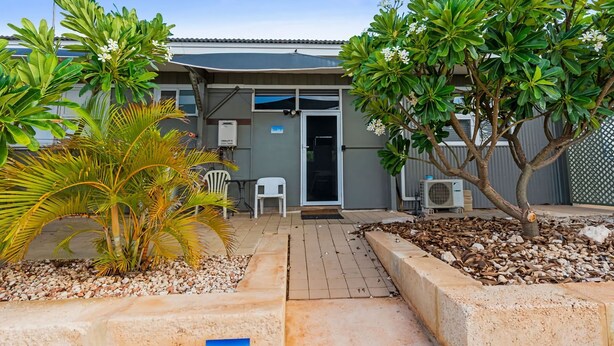 A residential property with a patio area, a small garden with palm plants, and a door leading to a covered entryway. - Getaway Villas Unit 38-7 - comfort on a budget (EXMOUTH)