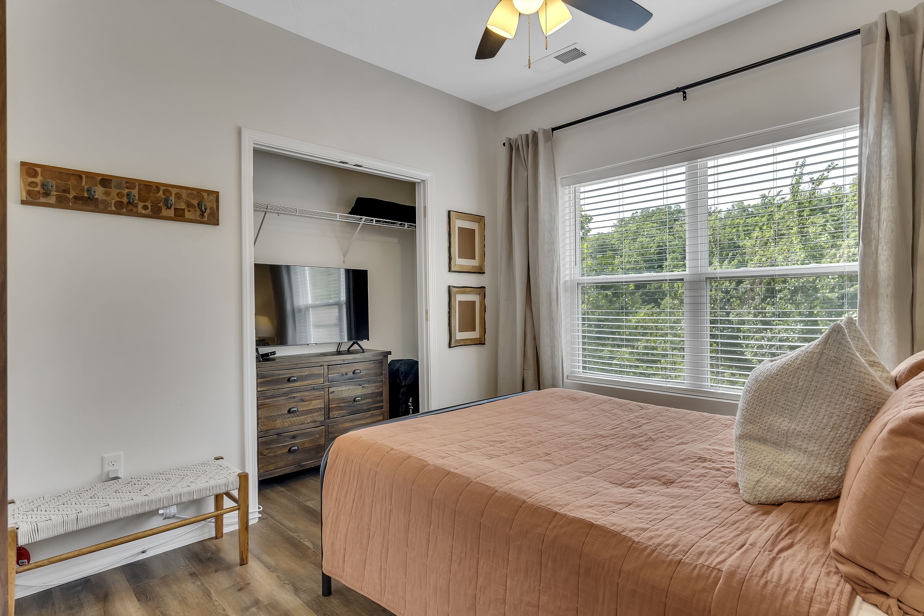 Een slaapkamer met een bed, een dressoir, een spiegel en een raam met jaloezieën.