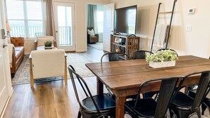 Ein geräumiges Wohnzimmer mit einem Holzessttisch, schwarzen Stühlen, einem Fernseher und einem Balkon mit Blick.