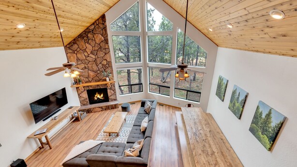 A spacious living room with a stone fireplace, large windows, and a wooden ceiling. - Built for large groups with luxury accommodations - An at home feel for everyone (Happy Jack)