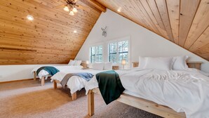 A cozy attic bedroom with two beds, wooden ceiling beams, and large windows. - Built for large groups with luxury accommodations - An at home feel for everyone (Happy Jack)