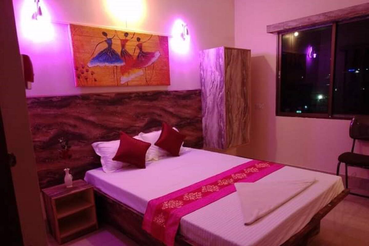 Ein Schlafzimmer mit einem hölzernen Kopfende, einem Bett mit weißen Laken und roten Kissen, einem rosa Teppichläufer und einem Gemälde über dem Bett.