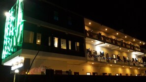 Un hotel a più piani con balconi su ogni livello, illuminato da luci interne.