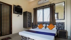 Un dormitorio con una cama, televisor, ventana con cortinas y espejo.