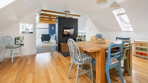 Un loft spacieux avec de hauts plafonds, un plancher en bois, une cheminée centrale et un coin repas comprenant une table et des chaises en bois.