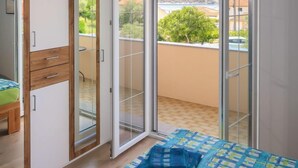 A bedroom with a sliding glass door leading to a balcony, a bed with a blue and green checkered bedspread, and a wooden wardrobe with drawers. - Apartment Mira by Interhome (Rab/Barbat)