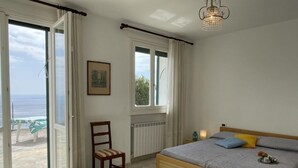Un dormitorio con cama, una silla, un ventanal y vista al mar.