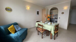 Un comedor con una mesa preparada para cuatro, un sofá azul con almohadones amarillos, y una cocina visible a través de un arco.