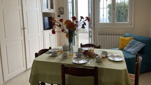 Un comedor con una mesa preparada para el desayuno, un florero con flores y vistas al exterior a través de las ventanas.