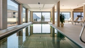 Ein moderner, überdachter Schwimmbereich mit gro ßen Glaswänden, Panoramafenstern und Bergblick.