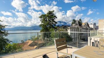 A terrace with a view of a lake and mountains, featuring a table and chairs.