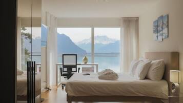 A bedroom with a bed, a desk, and a view of mountains and water.