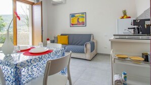 A modern kitchen with a coffee machine, a dining table with a blue patterned tablecloth, and a sofa with a gray and yellow cushion. - More e Lamponi by Interhome (San Giuliano Terme)