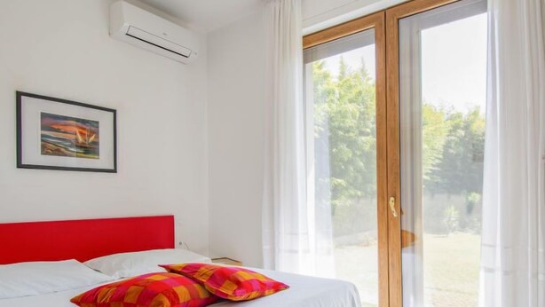 A bedroom with a bed, a red headboard, a framed picture on the wall, and a sliding glass door leading to an outdoor area. - More e Lamponi by Interhome (San Giuliano Terme)