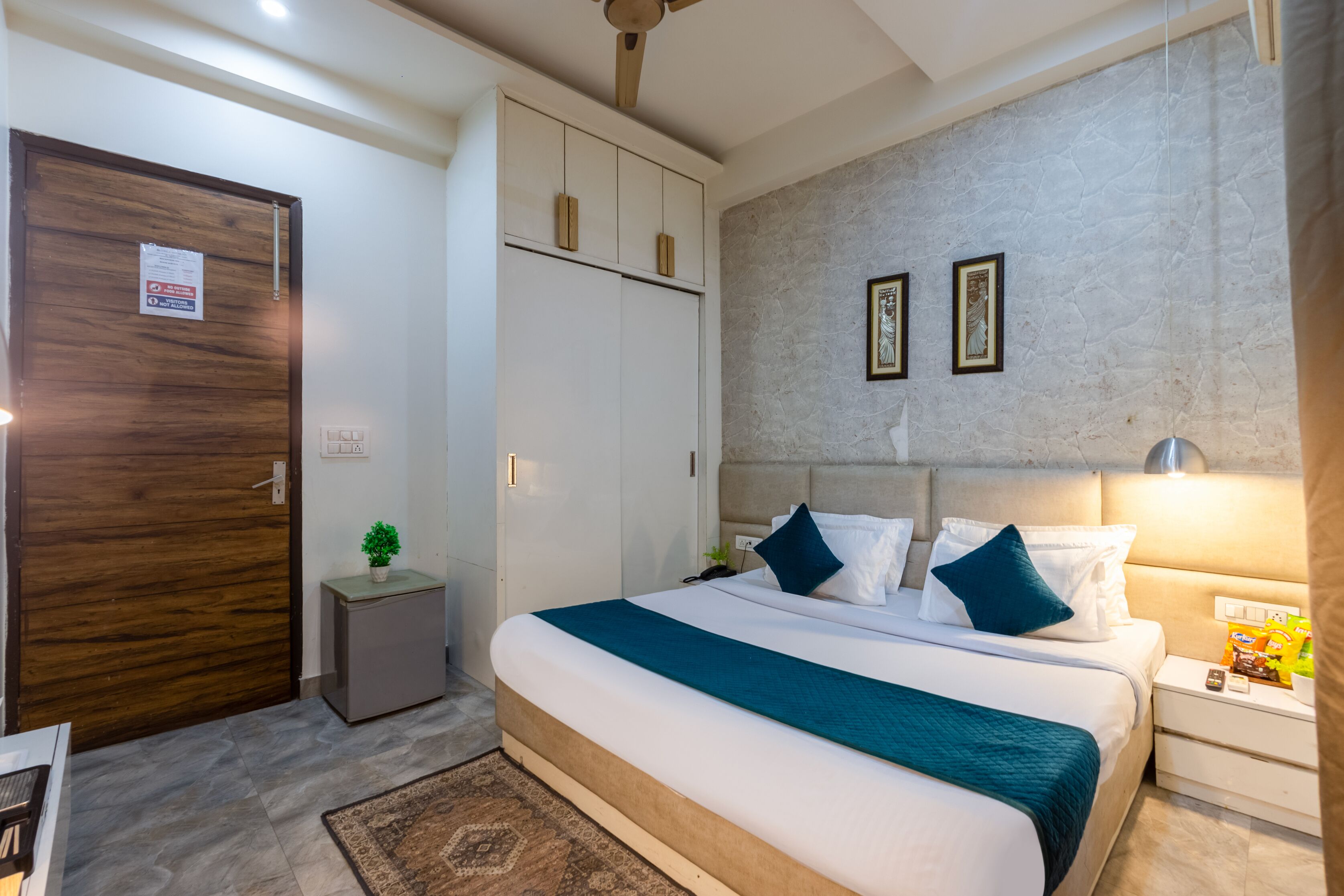A hotel room with a large bed, a wardrobe, a small bedside table, and a nightstand.