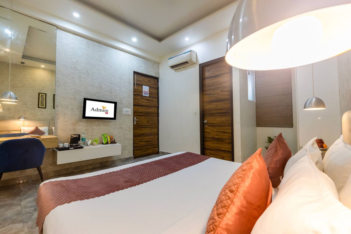 A hotel room with a bed, a TV mounted on the wall, a desk with a coffee machine, and a wardrobe.
